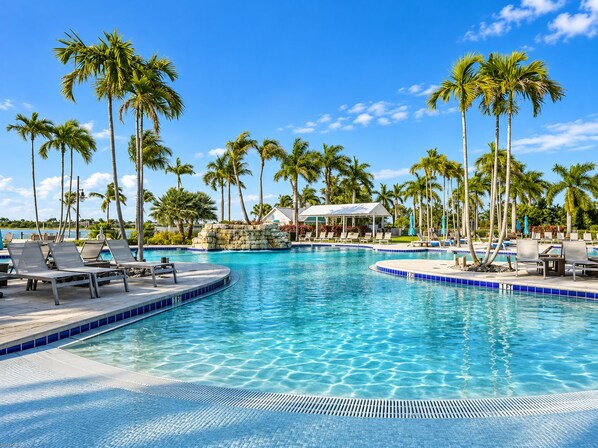A pool area with lounge chairs, palm trees, and a building in the background. - Lakeview Villa 2-bedroom 2 Bath plus den - pool! (Naples)