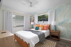 Ein Schlafzimmer mit einem Bett, einem Nachttisch, einer Lampe, einem Deckenventilator und einem Fenster mit Vorhängen.