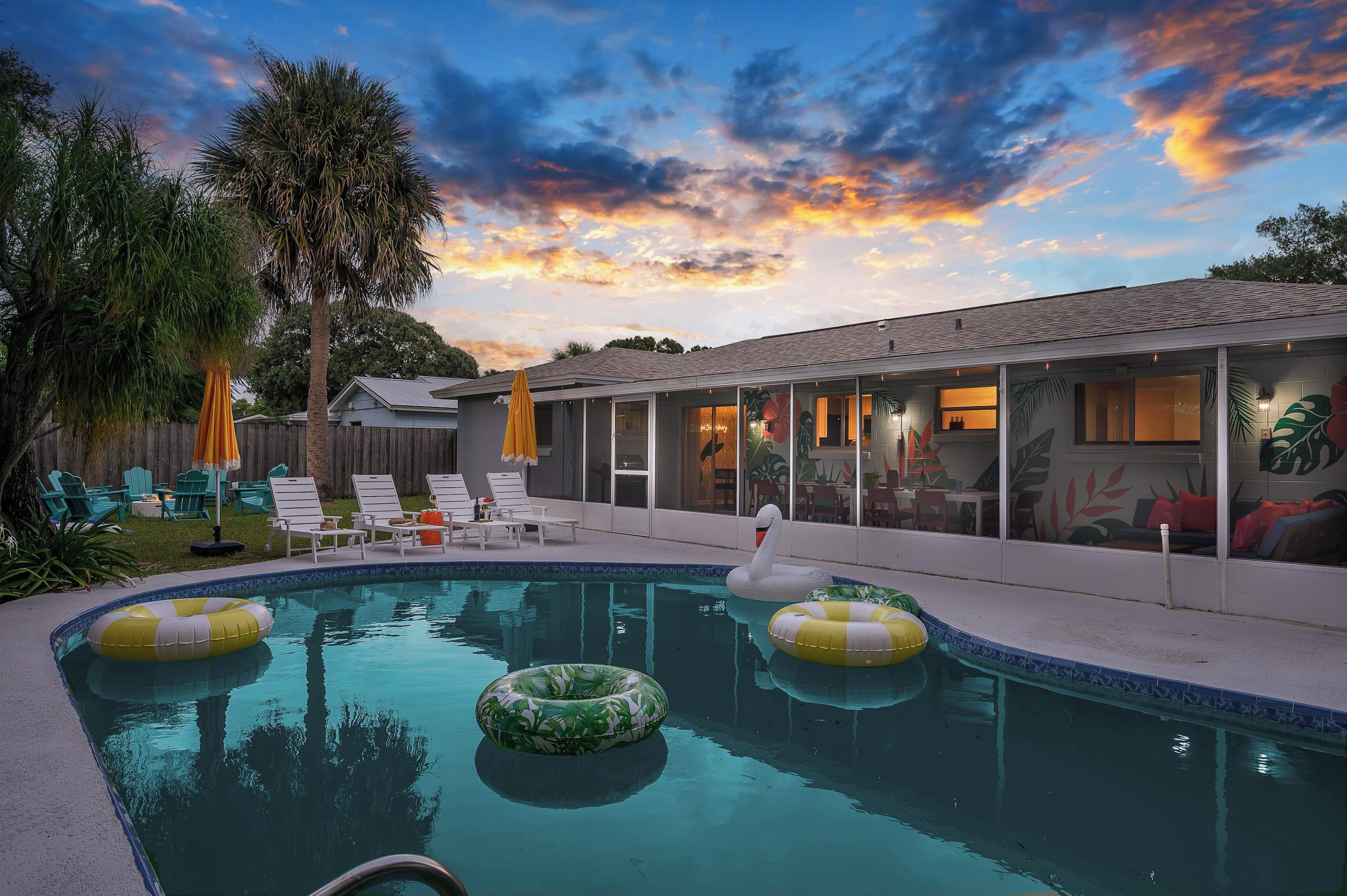 A backyard with a swimming pool, lounge chairs, and a house with a glass door.