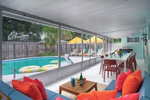 Ein überdachter Außenbereich mit Pool, Liegestühlen und einem Esstisch.