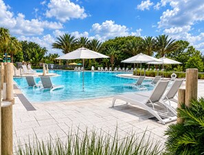 A swimming pool with lounge chairs and umbrellas, surrounded by palm trees and greenery. - Sunshine Hideaway Near Disney • Resort Pool • Family-Friendly 3BR (Davenport)