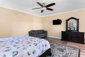 A bedroom with a bed, a gray sofa, a dresser, a ceiling fan, and a television. - Hospitality Expert VSV 9BR Chef Pool (Montego Bay)