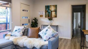 A living room with a grey sofa, a white furry throw blanket, and a potted plant.