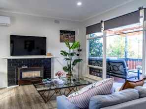 A living room with a fireplace, a flat-screen TV, a glass coffee table, and a sofa. - StayAU Cozy Getaway Near Westfield Knox (Wantirna South)