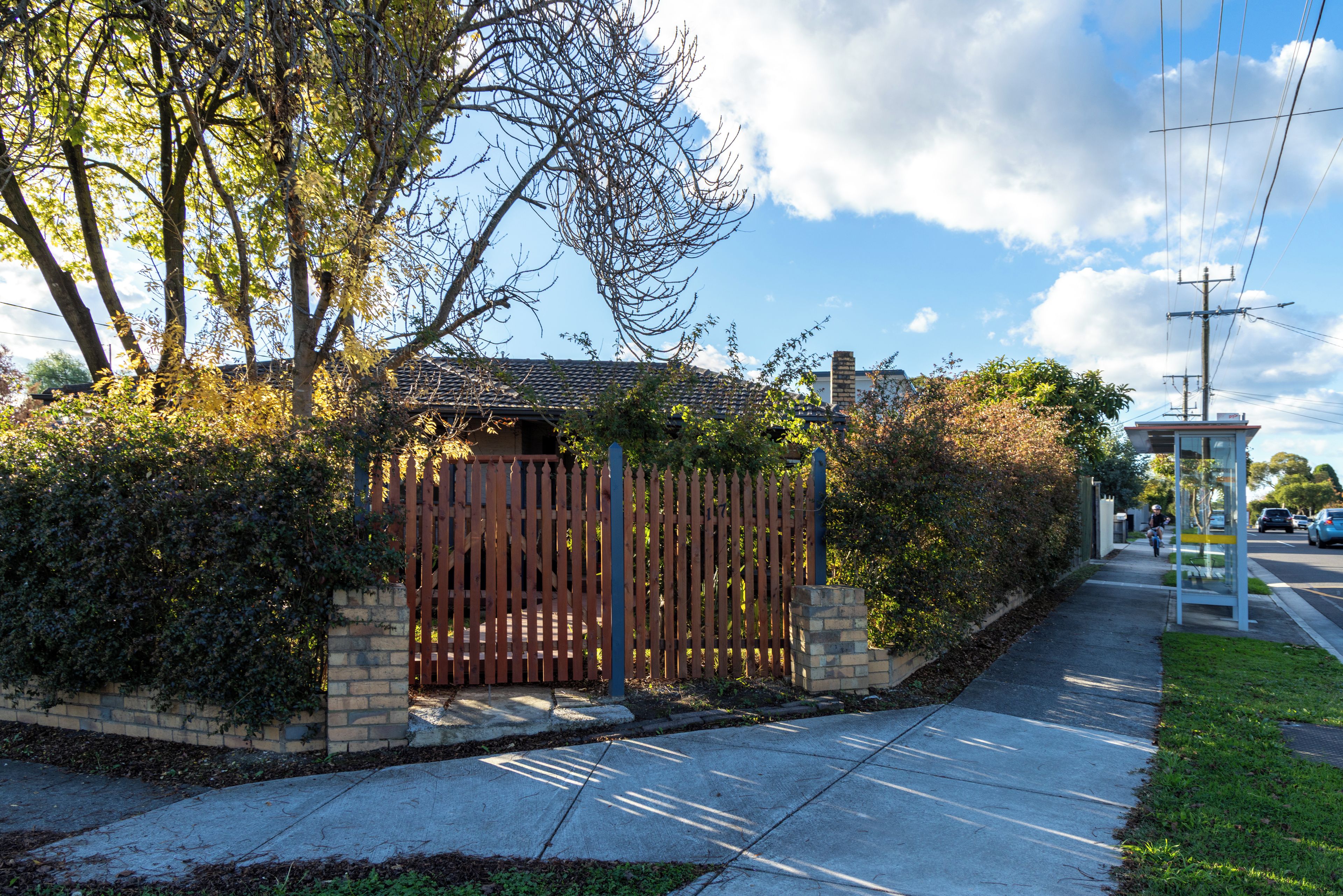 A gated entrance with a brick wall and wooden fence, a sidewalk, and a clear sky.