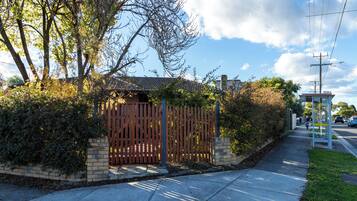 A gated entrance with a brick wall and wooden fence, a sidewalk, and a clear sky.