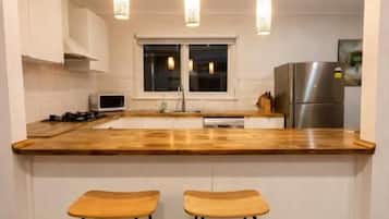 Une cuisine avec un plan de travail en bois, deux tabourets, des luminaires suspendus et un réfrigérateur.