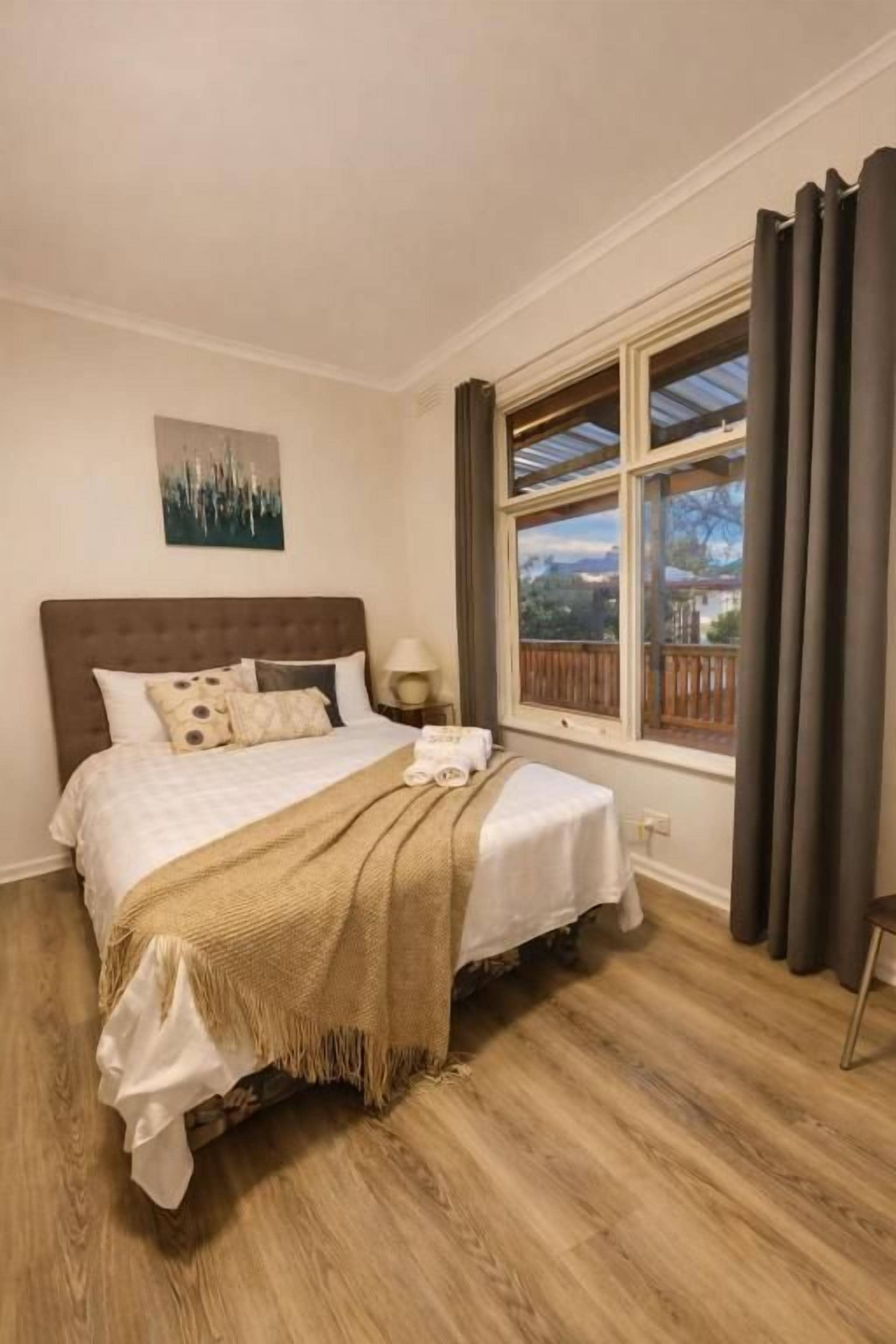 A bedroom with a bed, a nightstand, a window with curtains, and a view of the outdoors.