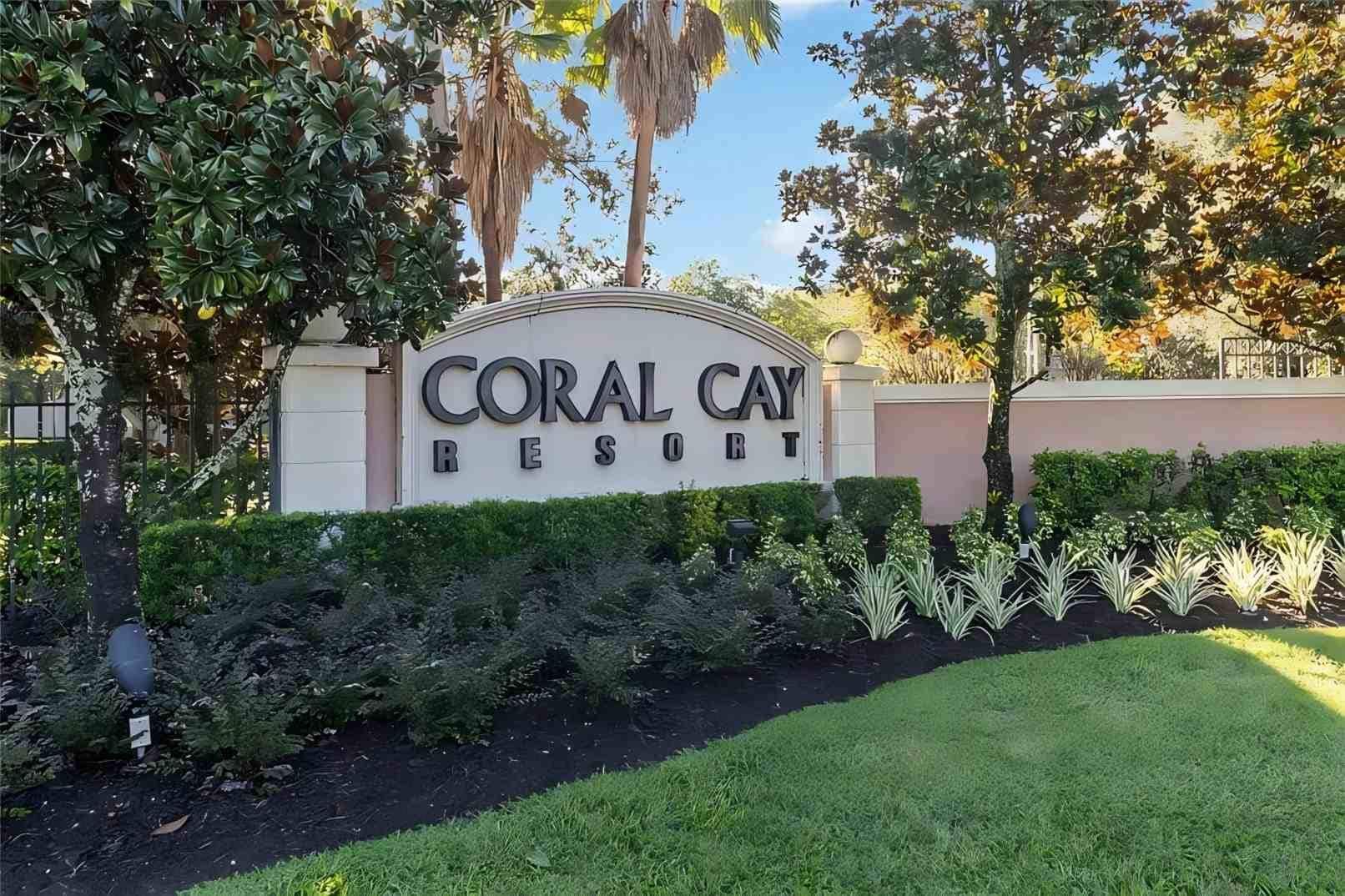 A sign for Coral Cay Resort with a landscaped garden in front.