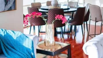A living room with a sofa, coffee table, and chairs. There is a dining area with a table and chairs in the background.