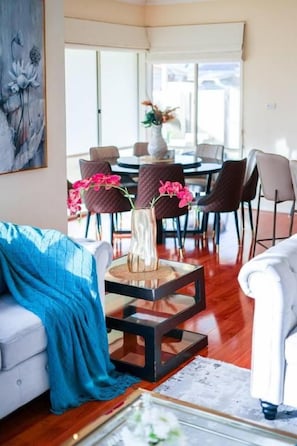Ein Wohnzimmer mit einer Couch, einem Couchtisch und Sesseln. Im Hintergrund ist eine Essecke mit Tisch und Stühlen zu sehen.