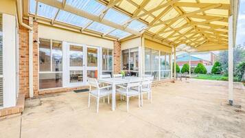 A covered patio area with a table and chairs, a brick wall, and a glass door.