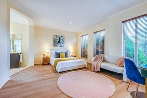 Ein Schlafzimmer mit einem Bett, Nachttischen, einem Sofa, einem Sessel und einem großen Fenster.