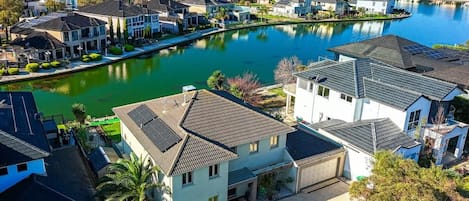 A residential area with houses along a water body, featuring a mix of single and multi-story buildings, some with solar panels.