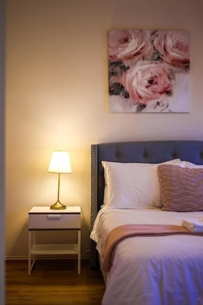 A bedroom with a bed, a nightstand, a lamp, and a floral painting on the wall.