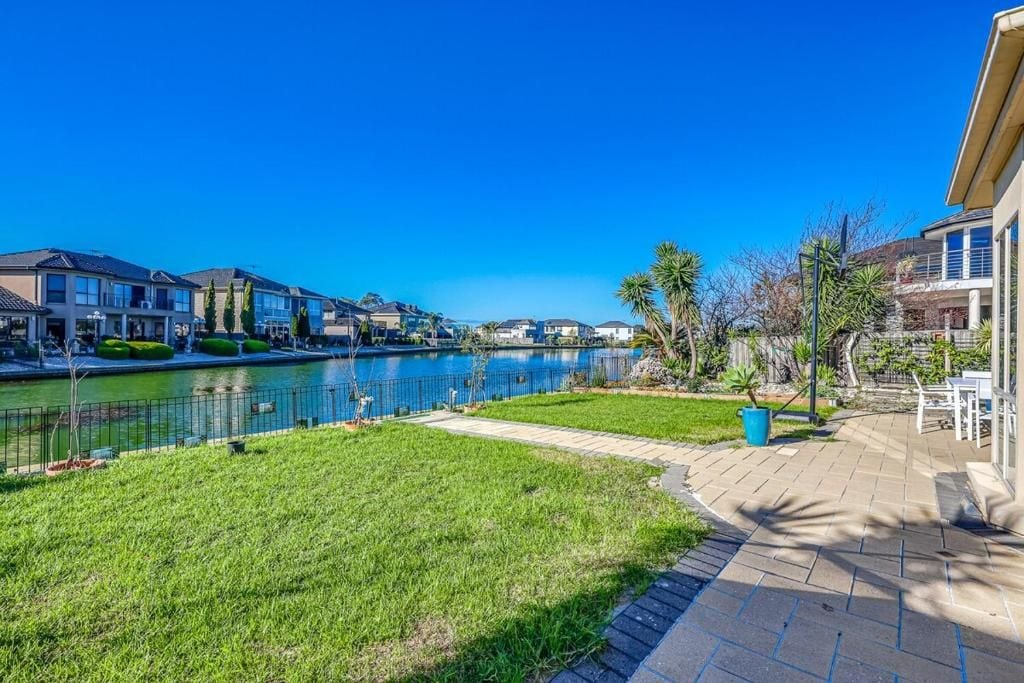 A residential area with a paved walkway, a small body of water, and houses with manicured lawns.