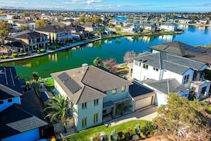 A residential area with houses along a water body, featuring a mix of single and multi-story buildings, some with solar panels.