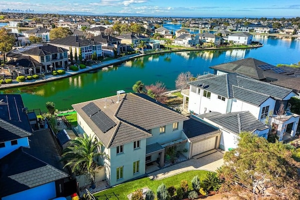 A residential area with houses along a water body, featuring a mix of single and multi-story buildings, some with solar panels.