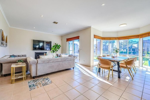 A spacious living room with a sofa, TV, and a dining area with chairs and a table.