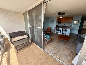Ein Zimmer mit einer Schiebetür zu einer Terrasse, einem Esstisch mit Stühlen, einer Couch und einer durch die Tür einsehbarer Küchenbereich.
