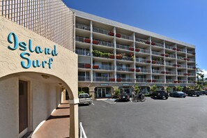 Ein mehrstöckiges Hotel mit Balkonen, einem Schild mit der Aufschrift 'Island Surf' und einem Parkplatz mit Fahrzeugen.