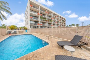 Ein Hotelpoolbereich mit blauem Wasser, Liegestühlen und einem mehrstöckigen Gebäude mit Balkonen.