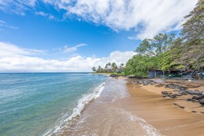 Une plage avec une eau claire, un rivage sablonneux et un bâtiment doté d’un toit et de fenêtres.
