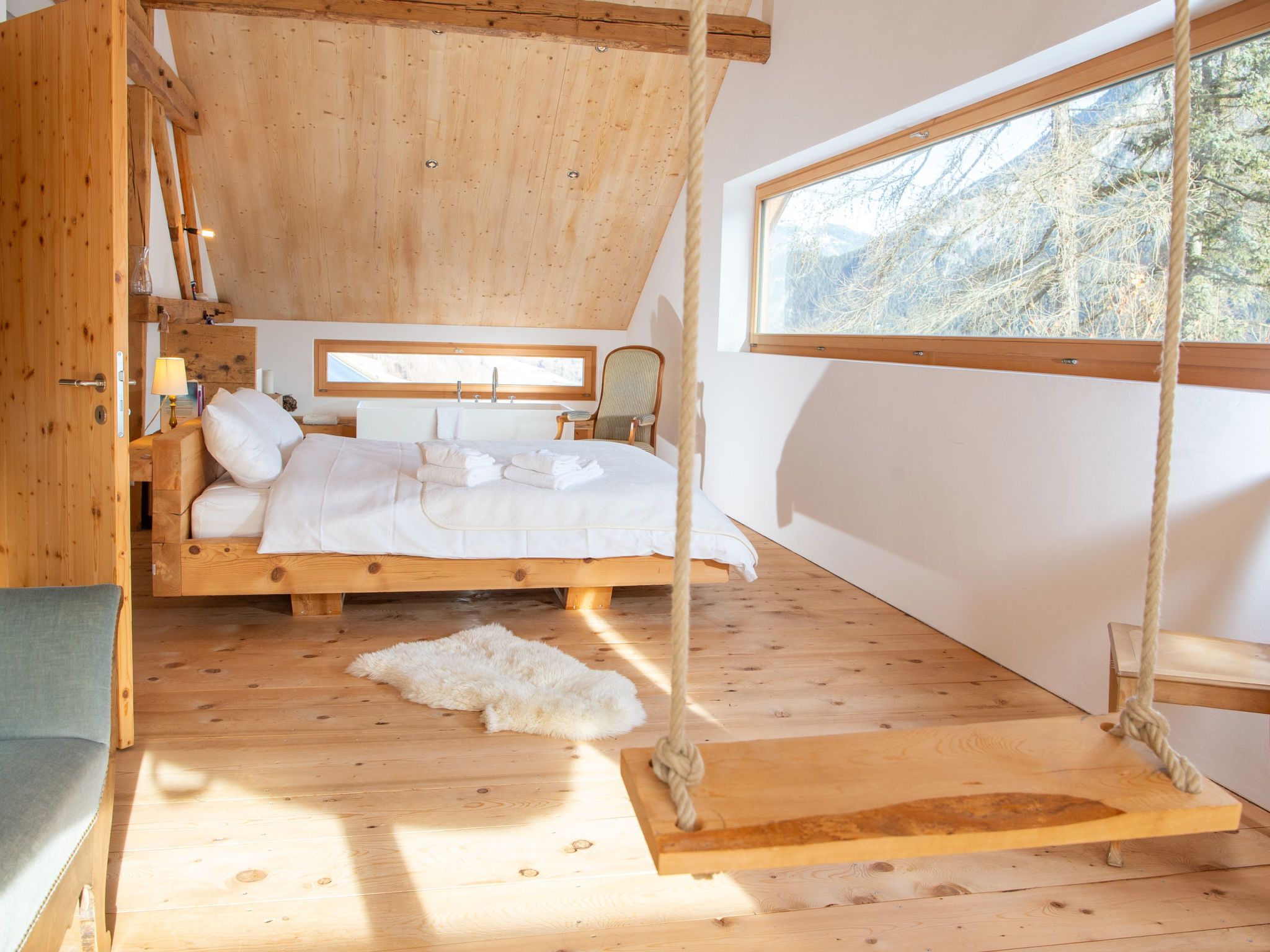 A wooden bedroom with a bed, a chair, a window, and a rope swing.