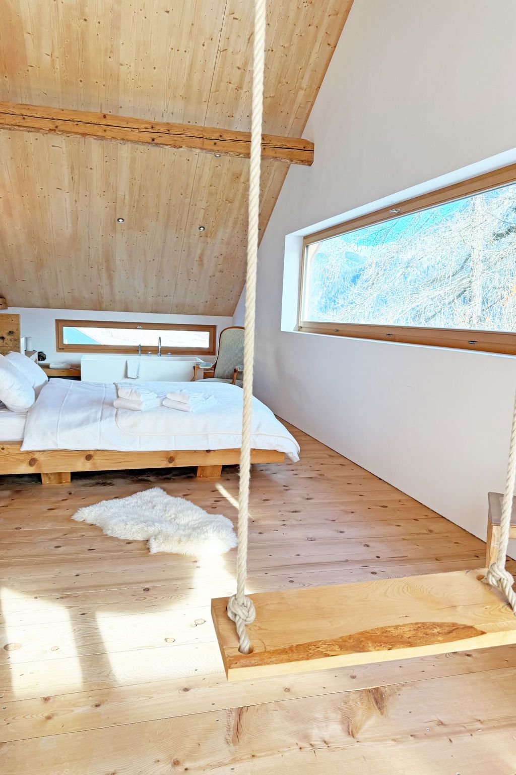 Ein Zimmer aus Holz mit einem Bett, einem Fenster und einer Hängematte.