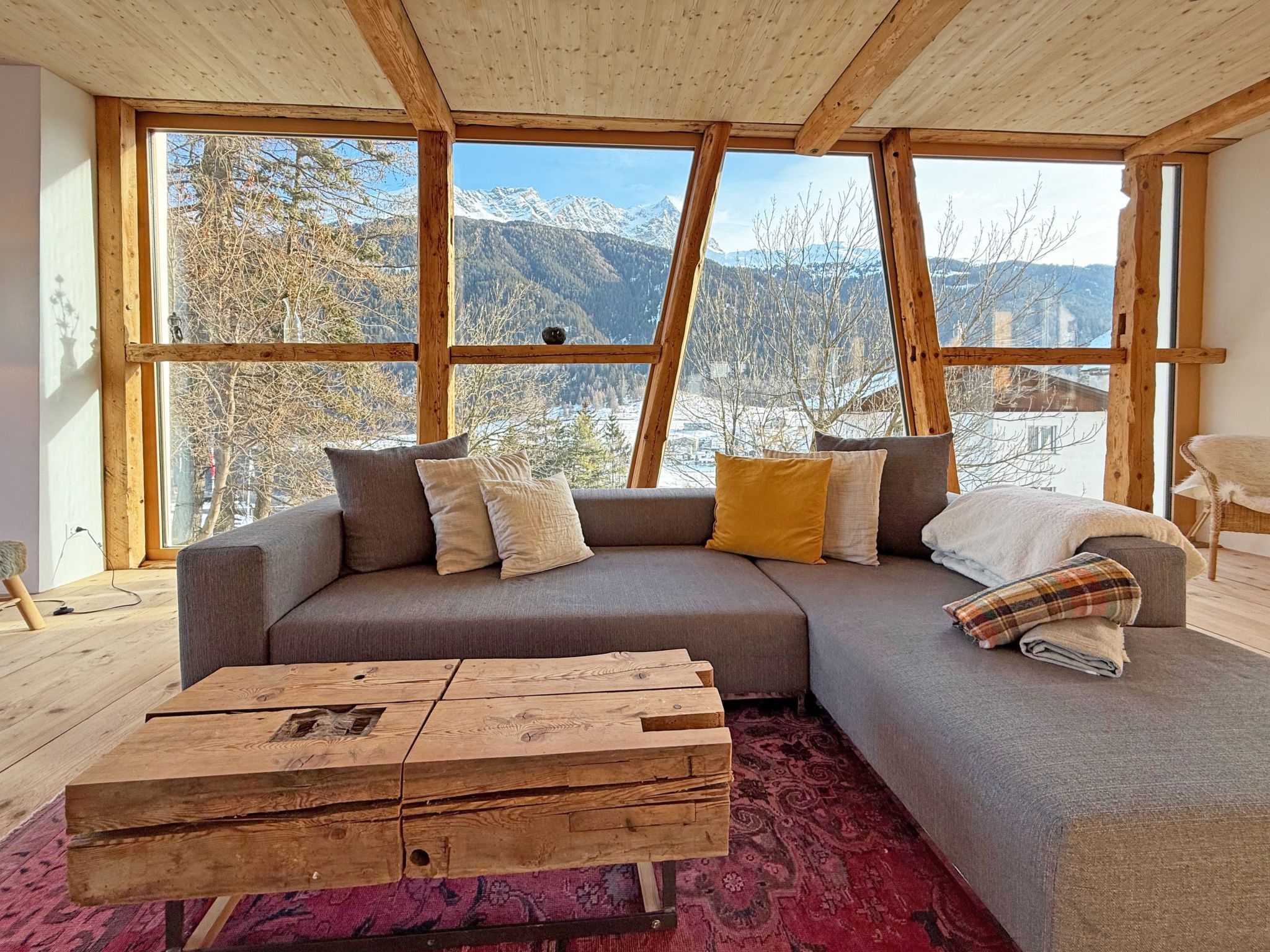 Una sala de estar moderna con un amplio sofá modular, una mesa de centro de madera y vistas a montañas a través de grandes ventanales.