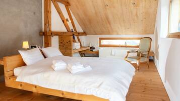 Un dormitorio con una cama de madera, una silla, una mesita y una ventana.