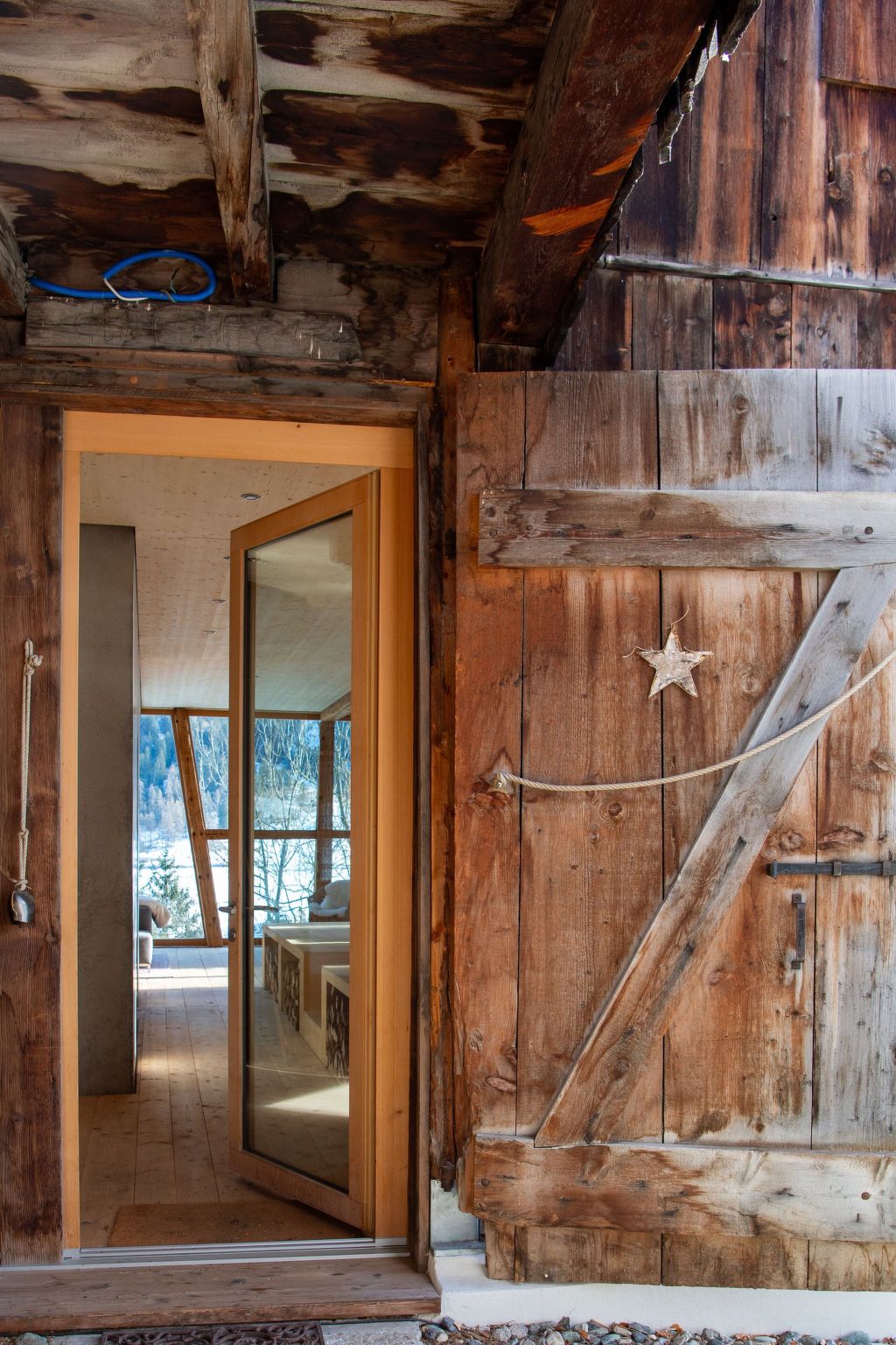 Un intérieur rustique en bois, avec une grande porte en bois, une vue dégagée sur l’extérieur et une corde attachée à la porte.