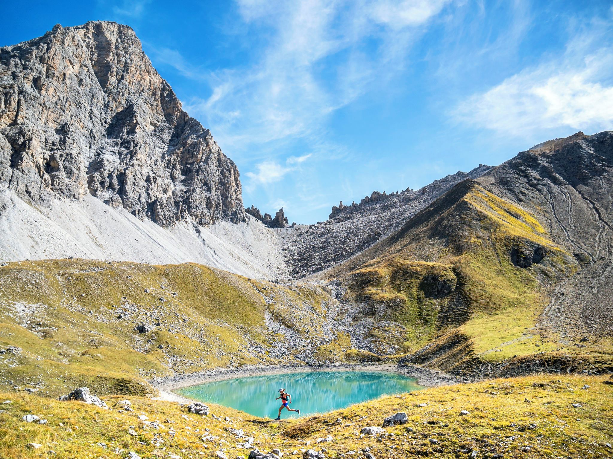 Eine Berglandschaft mit einem See und einer Person beim Laufen.