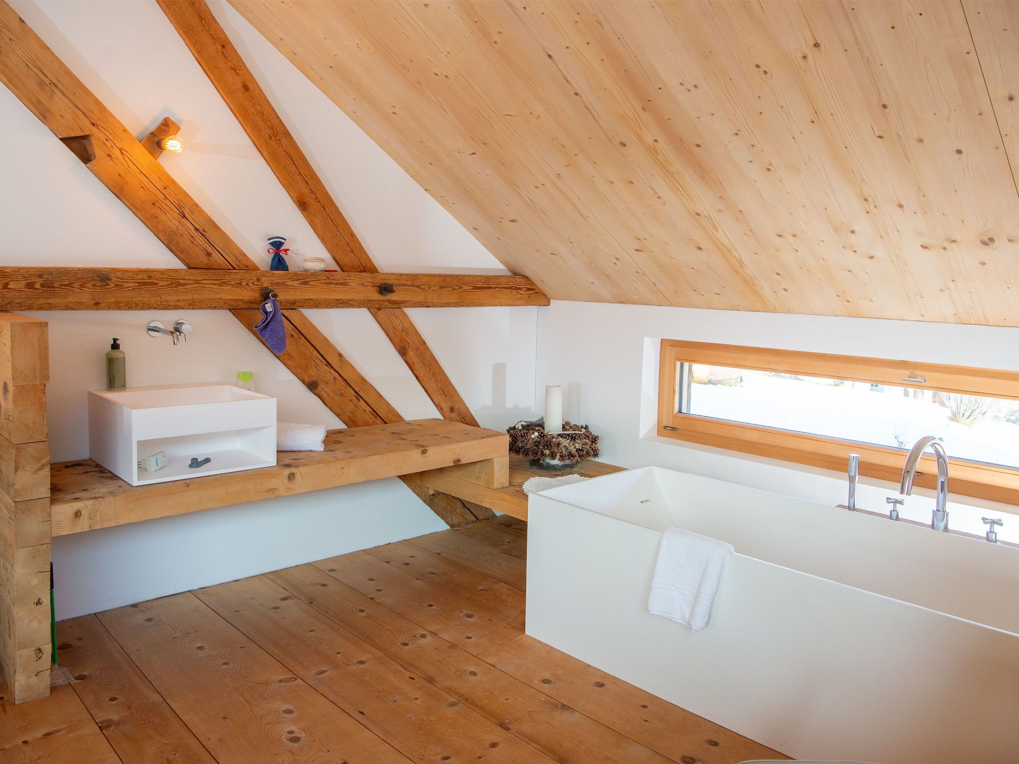 Ein modernes Badezimmer mit einer freistehenden Badewanne, Holzbalken, einem Fenster und einem Ablagefach für Pflegeprodukte.