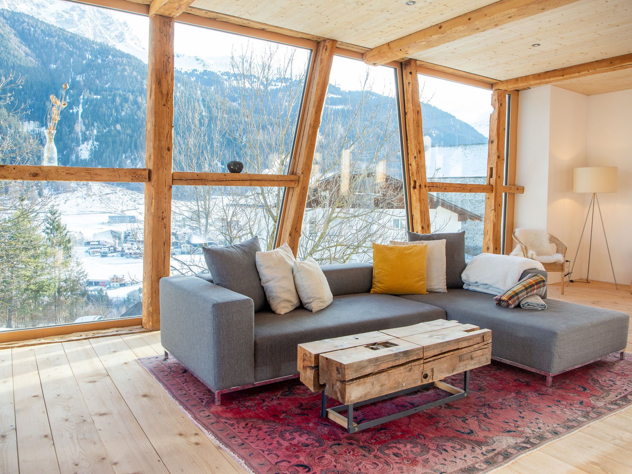 Ein modernes Interieur mit einem grauen Sofa, einem Holztisch und Blick auf verschneite Berge durch große Fenster.