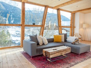 A modern interior with a grey sofa, wooden coffee table, and a view of snow-covered mountains through large windows.