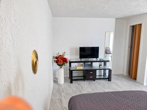 Ein Hotelzimmer mit einem Bett, einem Fernseher auf einem Glastisch, einer Vase mit Blumen und einem Spiegel an der Wand.