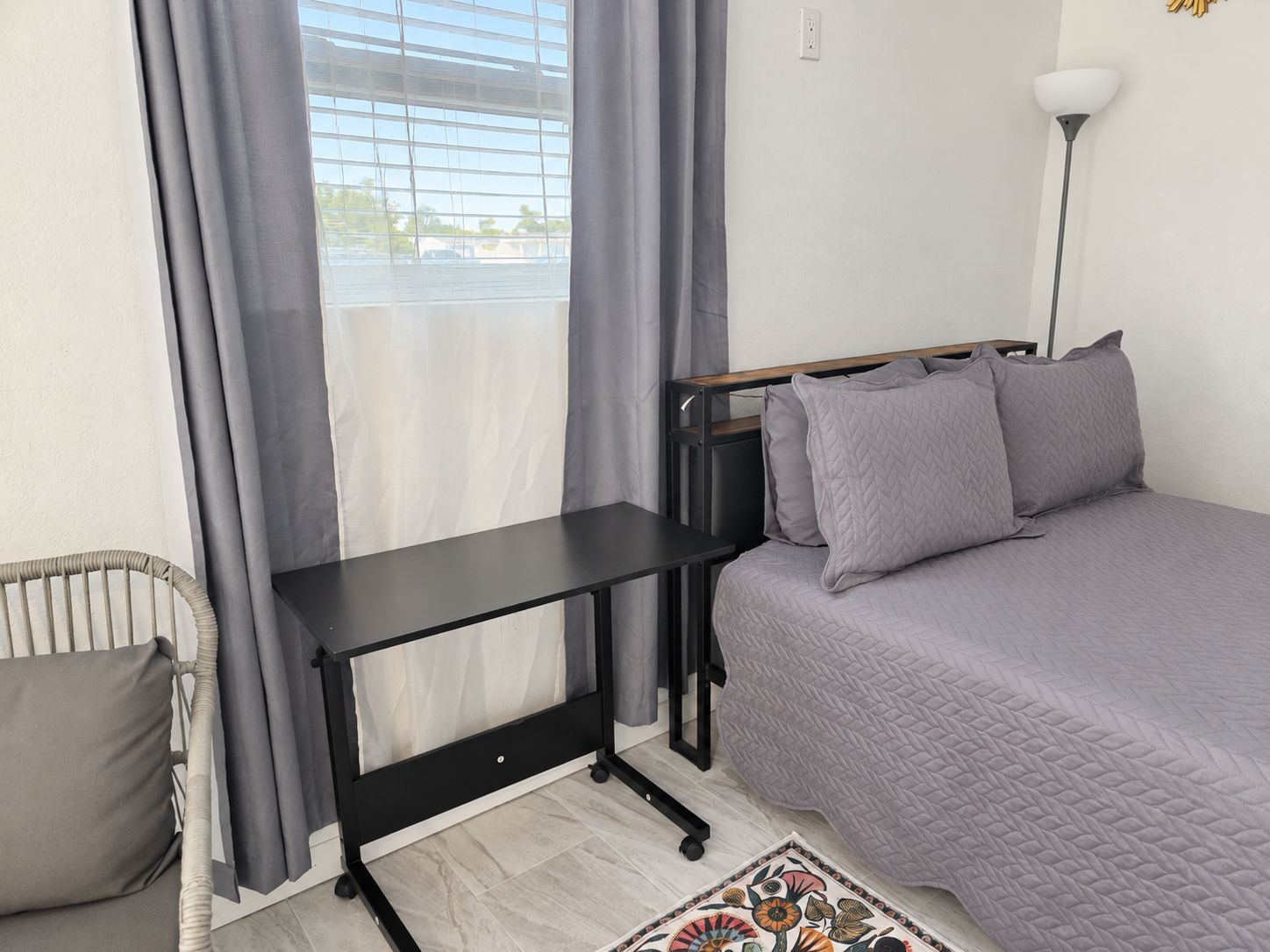Ein Zimmer mit einem Bett, einem Schreibtisch, einem Stuhl und einem Vorhangfenster.