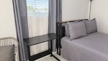Ein Zimmer mit einem Bett, einem Schreibtisch, einem Stuhl und einem Vorhangfenster.
