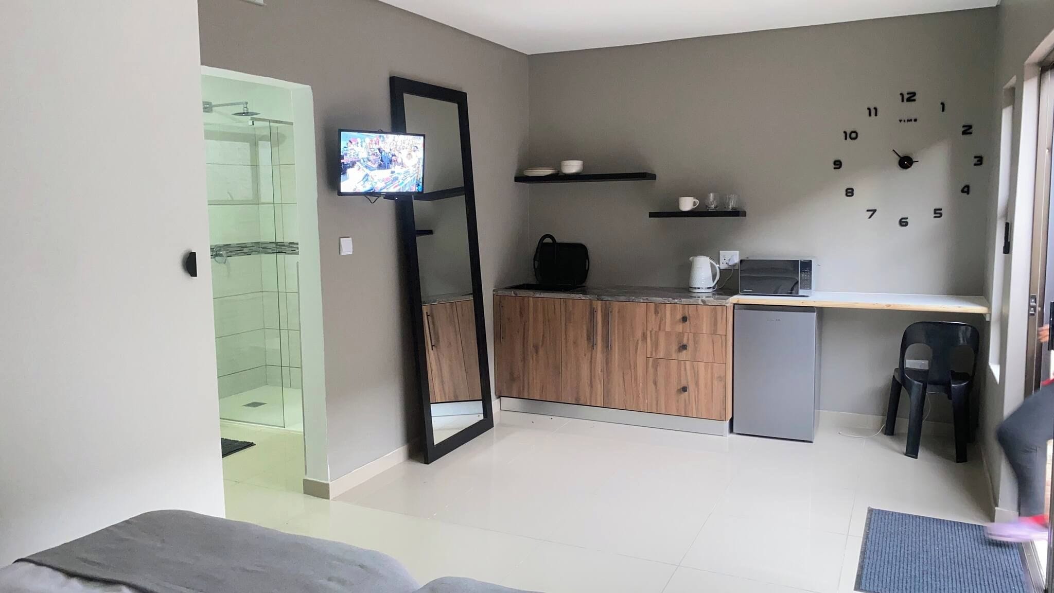 A compact living space with a kitchenette, a television mounted on the wall, and a door leading to a shower area.