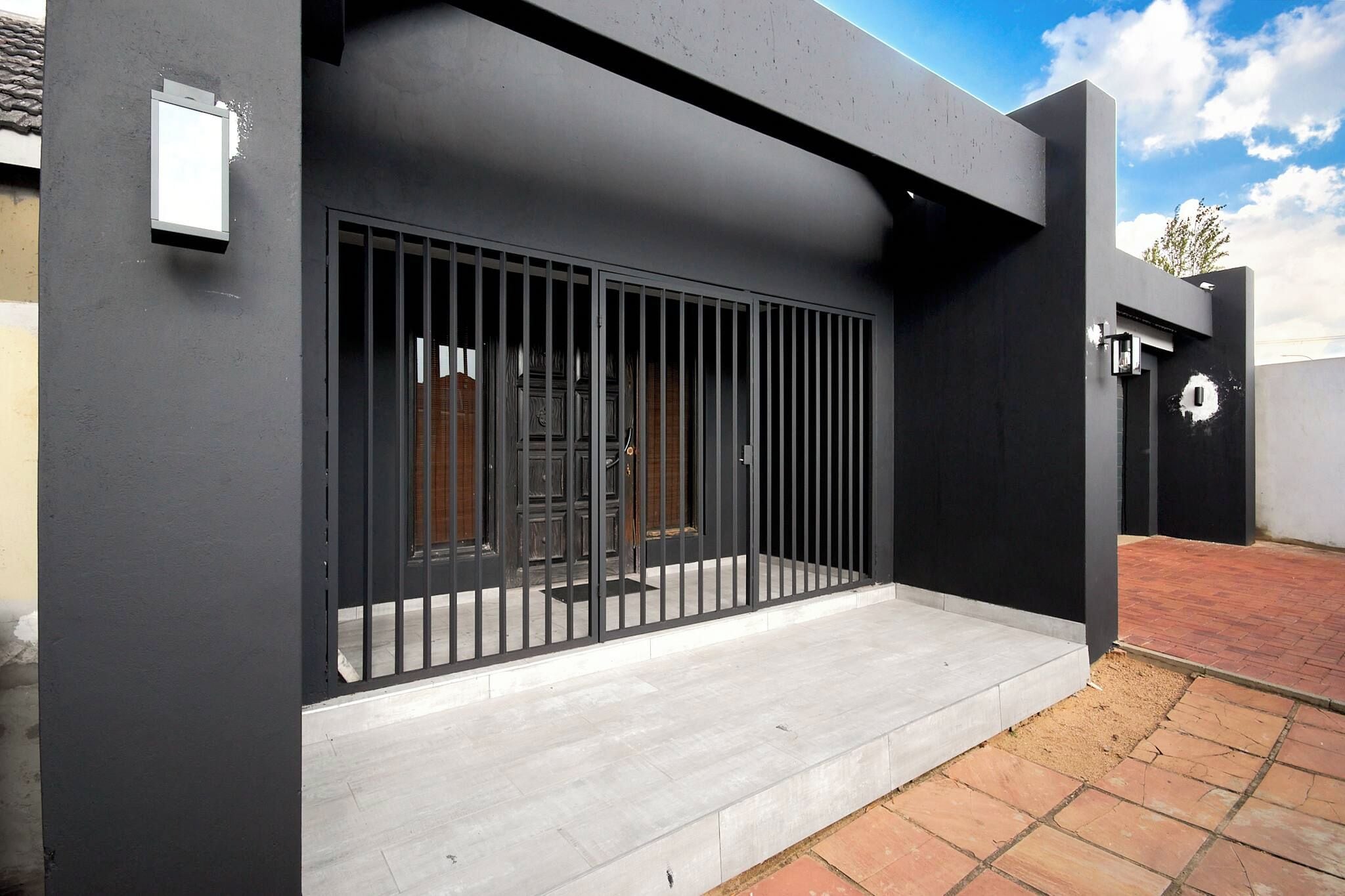 A modern building with a metal gate, a concrete entrance, and a paved area.