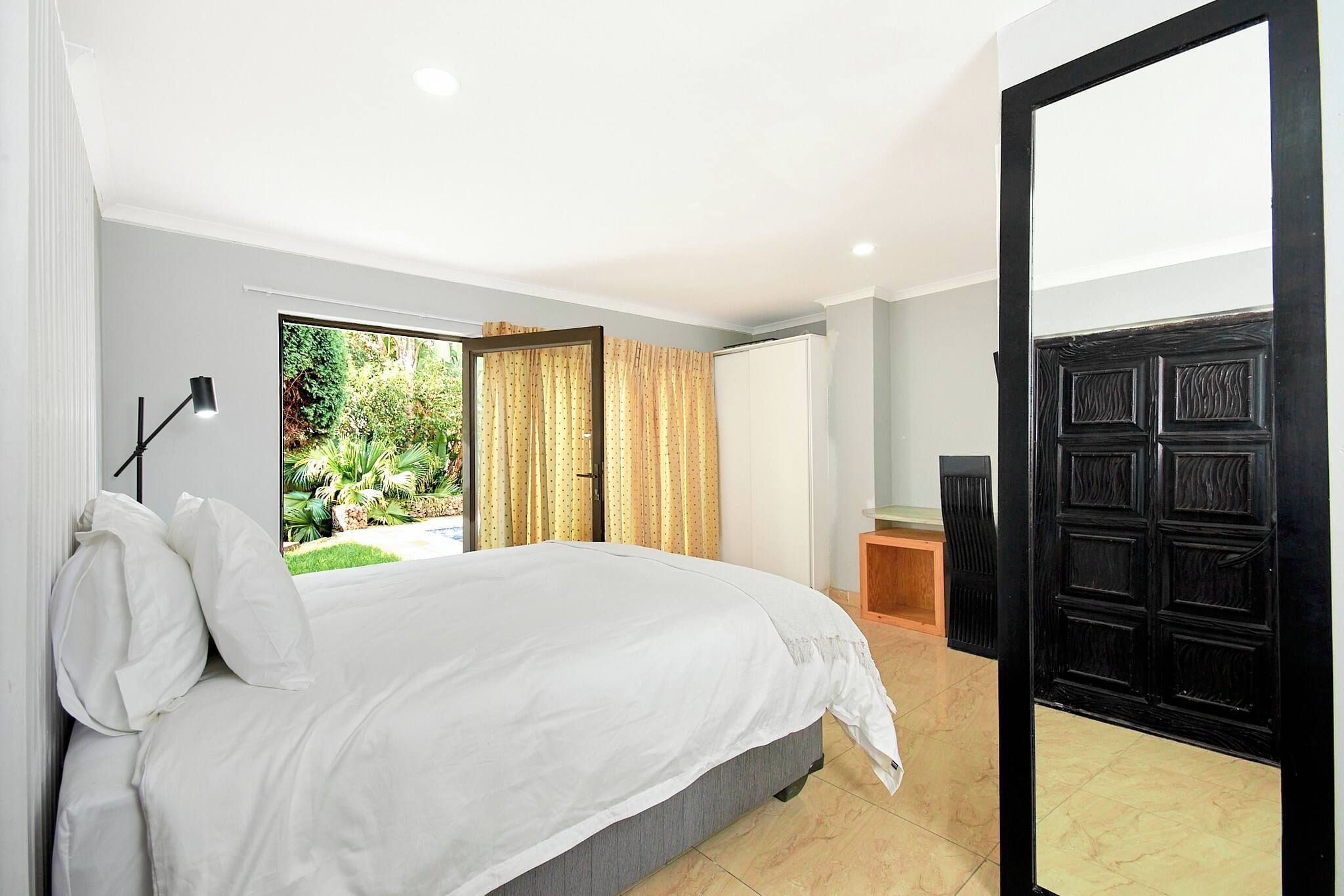 A bedroom with a bed, a desk, and a view of a garden.