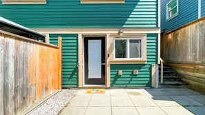 A green house with a wooden fence, a door, a window, and a small outdoor area with a mat. - Homely 1BR in Central Vancouver | 5mins walk to skytrain, 10 mins to DT (Vancouver)