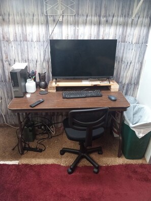 A home office setup with a computer desk, a large monitor, a keyboard, a mouse, and a chair. - 1 Bed 1 Bath Efficiency unit (North Platte)