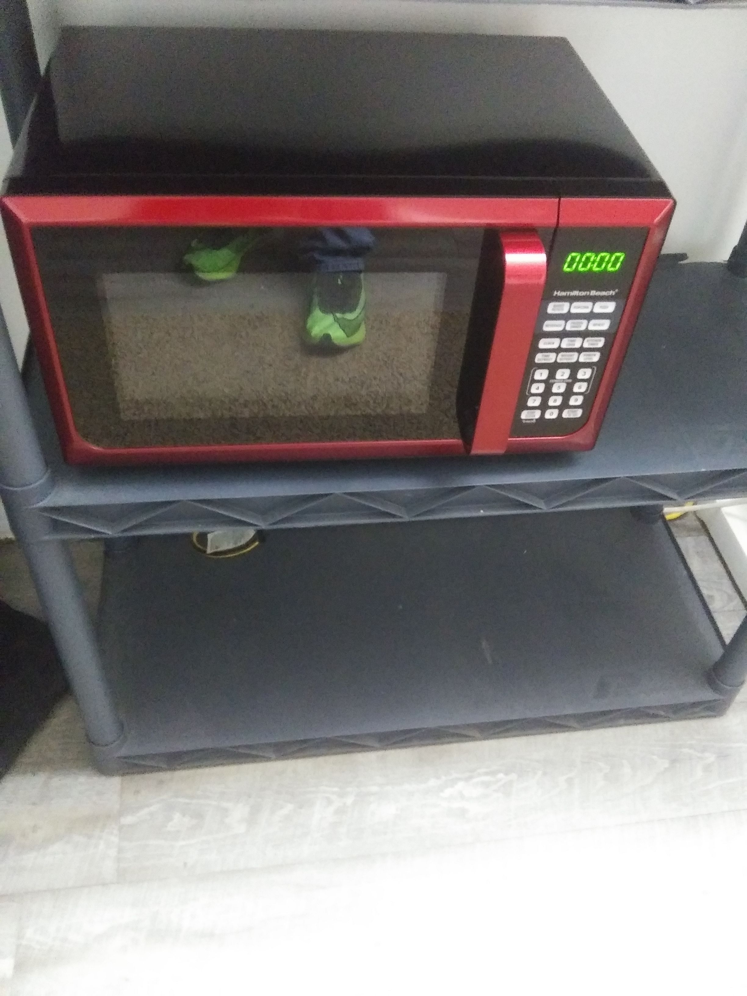 A red microwave oven on a black shelf.