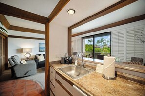 A modern kitchen with a granite countertop, stainless steel sink, and a window with a view of palm trees. - Aloha Sunrise | AC | POOL | HOT TUB (Koloa)