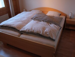 A neatly made bed with a wooden frame, two pillows with a checkered pattern, and a bedside table with a lamp. - Rottäli OG Appartement/Fewo, Dusche, WC, 2 Schlafräume 4-Bettwohnung by Interhome (Lenk)
