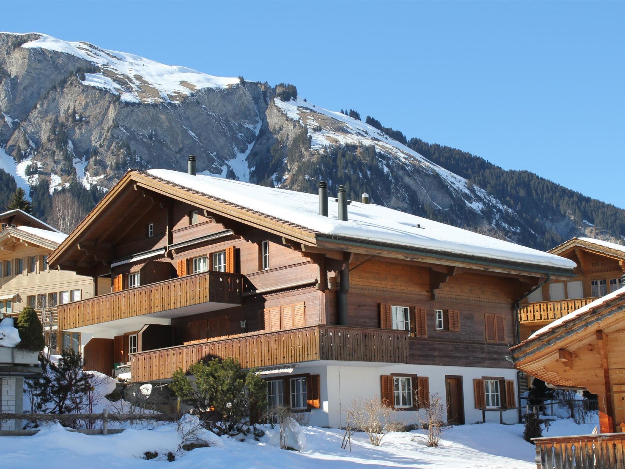 A wooden chalet with a balcony, set against a mountainous backdrop.
