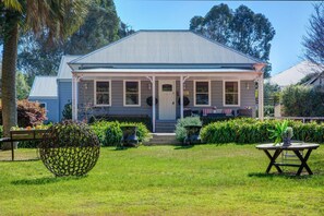 A two-story house with a front porch, a small garden, and a metal sculpture in the foreground. - Charming 1-Bed Cottage in Historic Berrima (Berrima)