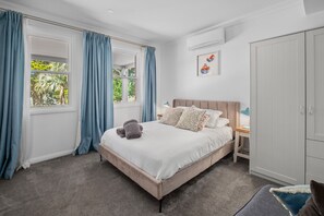 A bedroom with a bed, a nightstand, a wardrobe, and a window with curtains. - Charming 1-Bed Cottage in Historic Berrima (Berrima)